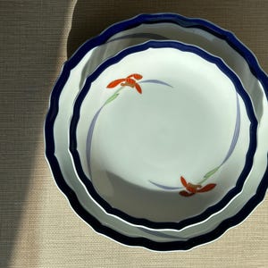 May include: Two white ceramic plates with a blue scalloped edge and a blue and orange floral design. The plates are stacked on top of each other, with the larger plate underneath.
