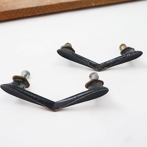May include: Two black metal drawer pulls with a V-shaped design and brass screws.