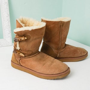 May include: A pair of brown suede boots with faux fur lining and buckle accents. The boots have a rounded toe and a low heel.