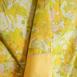Pode incluir: Tecido floral amarelo e verde com uma borda rosa. O tecido est&aacute; dobrado sobre si mesmo, mostrando o lado inferior amarelo.