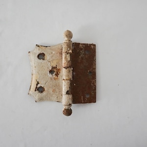 May include: A white and rusty metal hinge with a decorative finial. The hinge is in the shape of a rectangle with a rounded top and bottom.