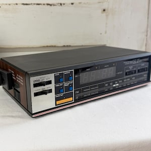May include: A vintage black and wood-tone Timex digital clock radio. The clock displays the time in red digits and has buttons for radio, time, and outlet control. The clock has a silver and red trim.