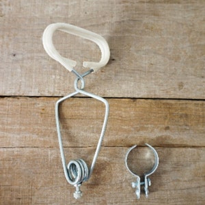 May include: A metal clothes hanger with a white plastic handle and a spring mechanism. A separate metal clip is also visible. The items are on a wooden surface.