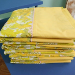 Pode incluir: Uma pilha de len&ccedil;&oacute;is de cama com padr&atilde;o floral amarelo e verde com acabamento rosa.
