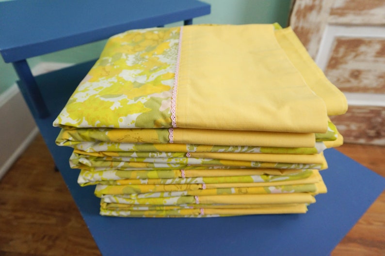 Pode incluir: Uma pilha de len&ccedil;&oacute;is de cama com padr&atilde;o floral amarelo e verde com acabamento rosa.