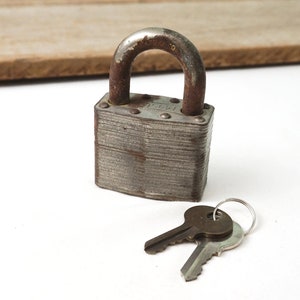 May include: A vintage silver padlock with two keys. The padlock has a rectangular shape and a rusty finish. The keys are silver and have a simple design.