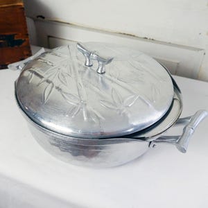 May include: A vintage silver-toned metal serving dish with a lid. The lid and handles feature a bamboo design. The dish is round with a lid that has a bamboo leaf pattern. The handles are shaped like bamboo stalks.
