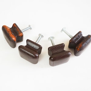 May include: Four brown wooden cabinet knobs with silver screws. The knobs have a unique shape with a dark brown finish and orange accents, perfect for adding a vintage touch to furniture. These knobs are ideal for a DIY project.