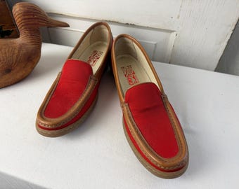 May include: Pair of red canvas loafers with brown leather trim. The shoes have a classic slip-on design and are set against a white background. The brand name "Ferragamo" is visible inside the shoe.