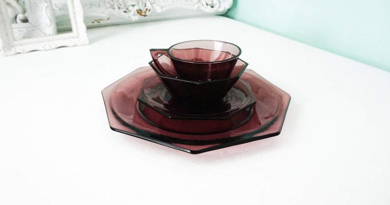 May include: A set of four purple glass plates and a cup, all with an octagonal shape. The plates are stacked on top of each other, with the cup on top of the smallest plate.