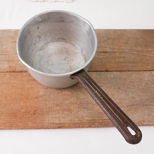 May include: A silver saucepan with a black handle. The saucepan is empty and sitting on a wooden surface.