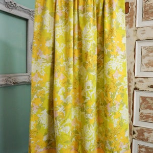 Pode incluir: Uma cortina amarela e verde com padr&atilde;o floral e uma borda inferior amarela. A cortina est&aacute; pendurada em um cord&atilde;o branco.