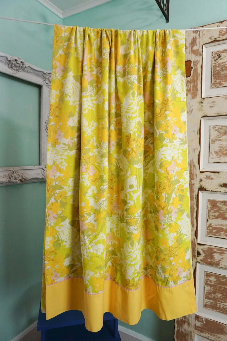 Pode incluir: Uma cortina amarela e verde com padr&atilde;o floral e uma borda inferior amarela. A cortina est&aacute; pendurada em um cord&atilde;o branco.