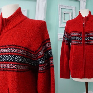 May include: Red knitted zip-up cardigan with a black, white, and gray geometric pattern.