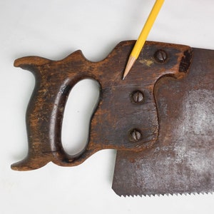 May include: A vintage hand saw with a wooden handle and a metal blade. The handle is dark brown and has a unique shape. The blade is rusty and has a serrated edge.