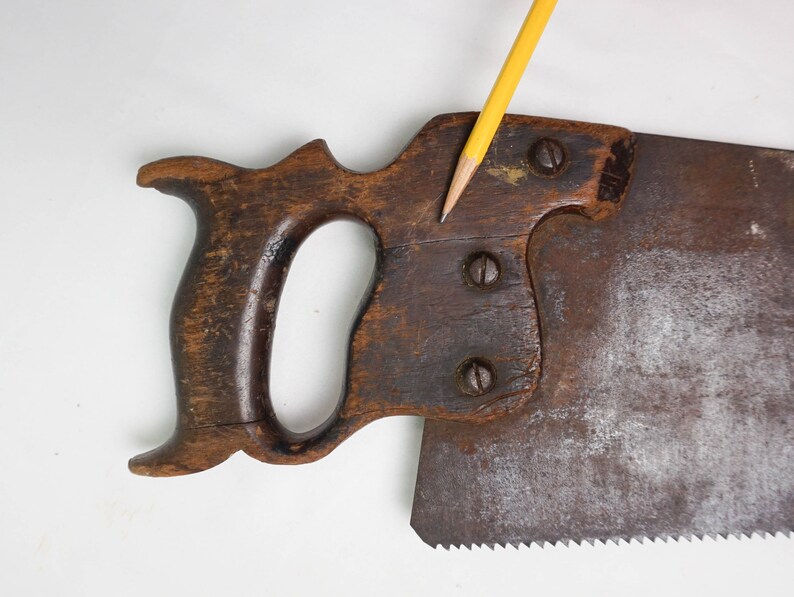 May include: A vintage hand saw with a wooden handle and a metal blade. The handle is dark brown and has a unique shape. The blade is rusty and has a serrated edge.