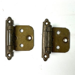 May include: Two antique brass cabinet hinges with a rounded top and a series of holes on the face. The hinges are in good condition with some signs of wear.