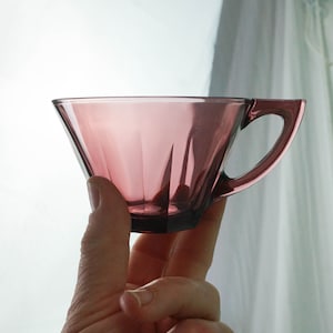 May include: A clear, purple glass teacup with a handle. The cup is shaped like a cone and has a fluted design.