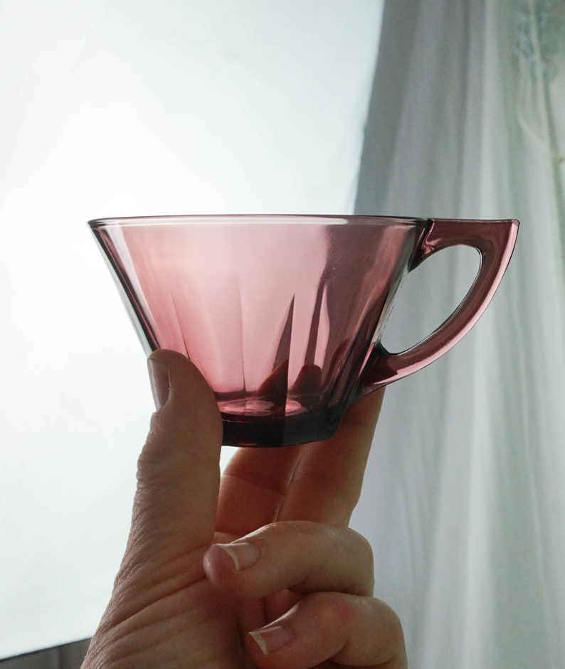 May include: A clear, purple glass teacup with a handle. The cup is shaped like a cone and has a fluted design.