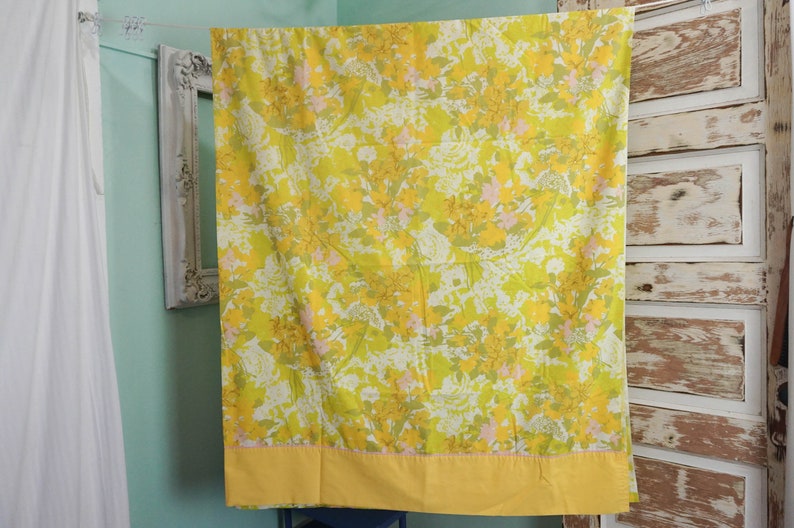 Pode incluir: Um len&ccedil;ol de cama com padr&atilde;o floral amarelo e verde com uma borda amarela. O len&ccedil;ol est&aacute; pendurado em um varal.