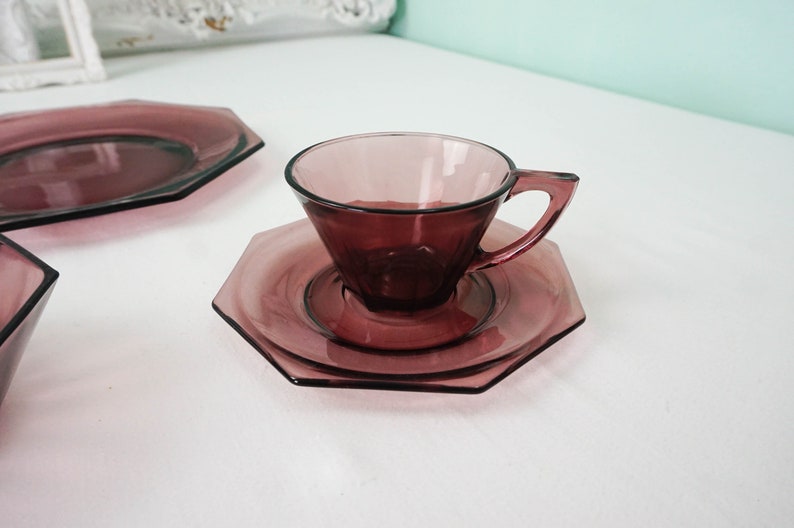 May include: A set of purple glass teacups and saucers with an octagonal shape. The cups and saucers are made of clear glass with a purple tint.