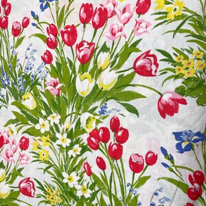 May include: A white fabric with a floral print featuring red, pink, white, yellow, and blue flowers. The flowers are tulips, daffodils, and other spring blooms.