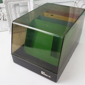 May include: A black plastic storage box with a clear lid. The box has a green interior and a label that reads "REV MODEL/75".