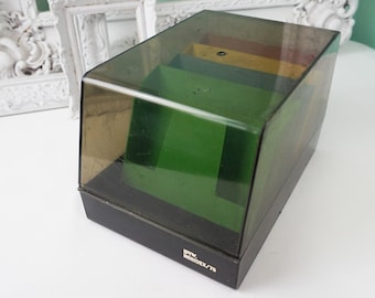 May include: A black plastic storage box with a clear lid. The box has a green interior and a label that reads "REV MODEL/75".