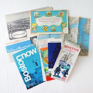 May include: A collection of vintage travel ephemera, including maps and brochures. The items feature text such as "Massachusetts", "Boston", and "Boston Vicinity". The color palette includes blue, white, and gray.