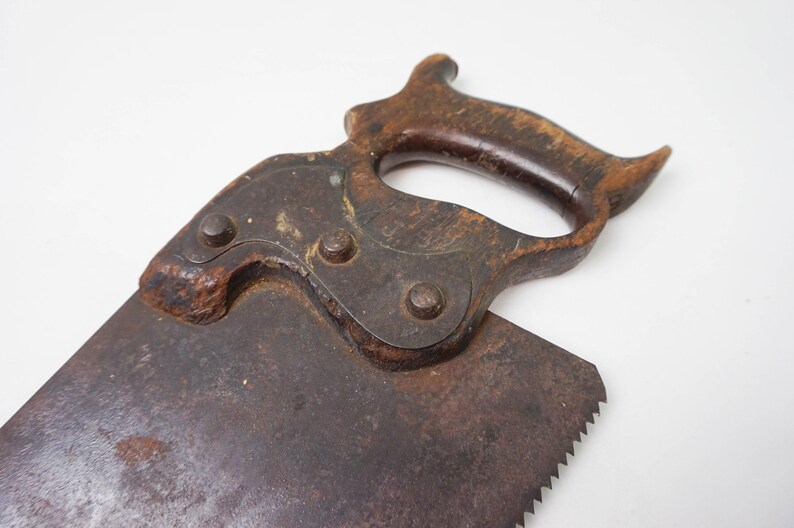 May include: Close-up of the wooden handle of an antique saw. The handle is made of dark wood and has a unique shape. The saw blade is made of metal and has a rusty patina.