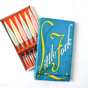 May include: A set of six colorful forks in a box. The forks are made of stainless steel and have plastic handles with the words "Stay Sweet" printed on them. The box is blue with the words "Little Fork" printed in yellow.