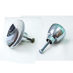 May include: Two silver door knobs with a screw attachment. One knob is round and the other is a flat disc.