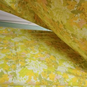 Pode incluir: Tecido amarelo com um padr&atilde;o floral em tons de amarelo, verde e rosa. O tecido est&aacute; dobrado ao meio, criando uma forma triangular.