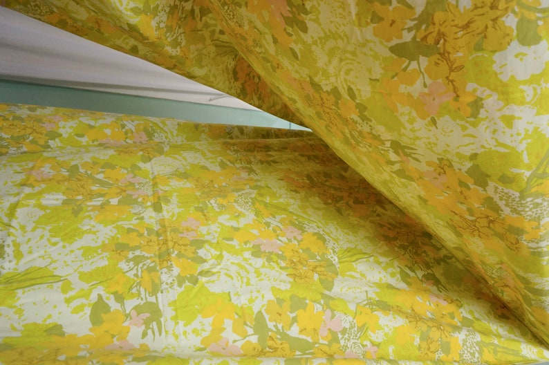 Pode incluir: Tecido amarelo com um padr&atilde;o floral em tons de amarelo, verde e rosa. O tecido est&aacute; dobrado ao meio, criando uma forma triangular.