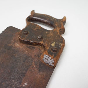 May include: A vintage hand saw with a wooden handle and a rusty blade. The handle has a metal plate with the inscription "HK".