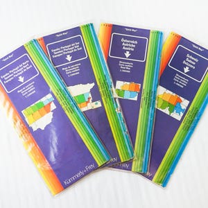 May include: A collection of travel maps with a purple background and colorful stripes. The maps are labeled in multiple languages, including English, French, and German. The maps are from the publisher Kümmerly+Frey.