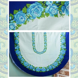 May include: A white tablecloth with a blue and green floral pattern. The tablecloth has a scalloped edge and is decorated with a row of blue roses around the perimeter.