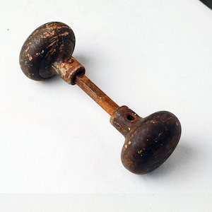 May include: An antique door knob with a dark brown, weathered finish. The knob has two rounded ends connected by a slender, aged metal rod. The hardware shows signs of wear, suggesting its vintage nature. A classic piece for home decor.