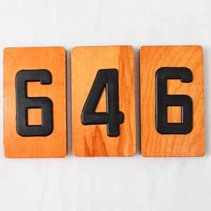 May include: Three wooden blocks with black numbers on them, spelling out the number 646.