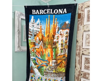 Pode incluir: Uma toalha de praia preta com uma imagem colorida da Sagrada Família, um famoso marco de Barcelona, Espanha. A toalha tem a palavra "Barcelona" impressa em branco no topo.