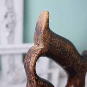 May include: Close-up of a wooden hand plane with a dark brown finish. The handle is shaped like a bird's head with a small hole in the top.