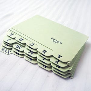 May include: A stack of light green index cards with black lettering. The cards have alphabetical tabs, with letters like A, B, C, and Z. The text "GLOBE-WEIS" is printed on the side of the cards.