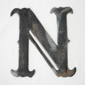 May include: A black metal letter N with a distressed finish. The letter is made of thick metal and has a slightly rustic look.