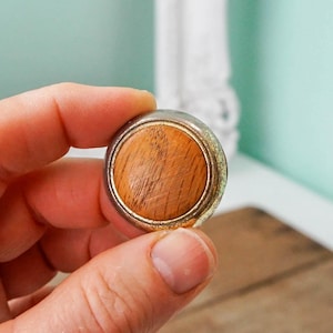 May include: A round wooden knob with a silver metal rim. The knob has a wood grain pattern and is slightly worn.