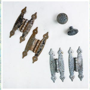 May include: A set of antique door hinges and knobs. The hinges are made of metal and have a distressed finish. The knobs are round and have a textured surface. The hinges and knobs are in various shades of silver and gray.