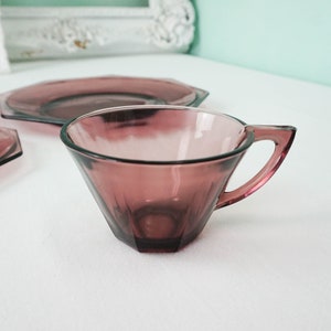 May include: A set of purple glass teacups and saucers. The teacups and saucers have a geometric, octagonal shape.