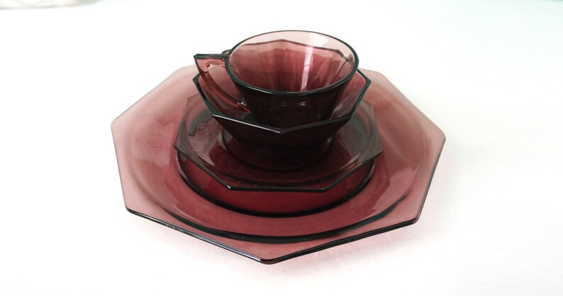 May include: A set of four octagonal glass plates and a cup in a deep purple color. The plates are stacked on top of each other, with the cup on top of the smallest plate.