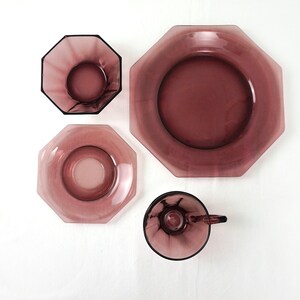 May include: Set of four purple glass dishes in an octagonal shape. The set includes a large plate, a smaller plate, a saucer, and a cup.