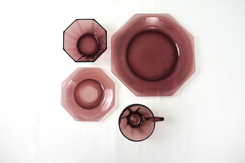 May include: Set of four purple glass dishes in an octagonal shape. The set includes a large plate, a smaller plate, a saucer, and a cup.