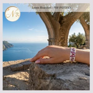 May include: A loom bracelet featuring a white background with a pink butterfly design and small floral accents. The bracelet is secured with gold-toned metal end bars. The text "Loom Bracelet / PDF PATTERN" is visible at the top of the image.